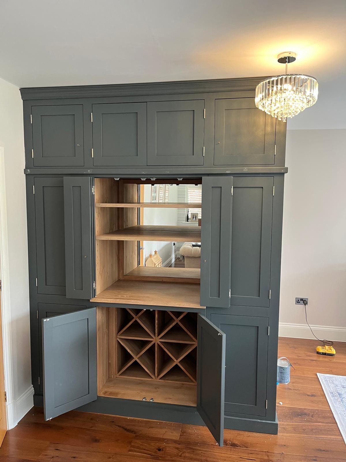 Open dark painted drinks cabinet showing wooden shelving, a mirror and wine storage