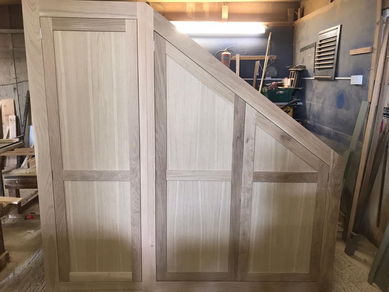 Unfinished wooden under-stairs cupboards with angled panelled doors in the workshop